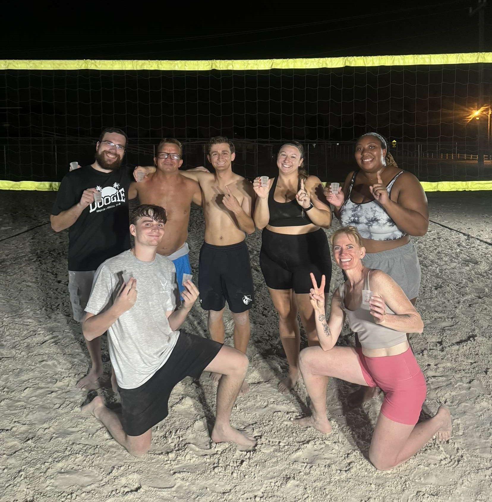 A group of people are posing for a picture in front of a volleyball net.