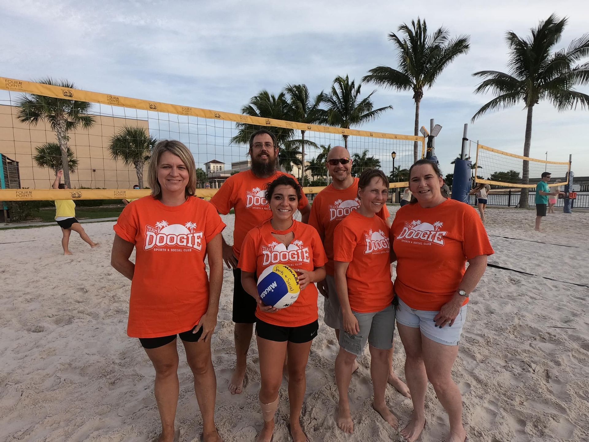 A group of people are posing for a picture on a beach while wearing orange shirts that say duckie