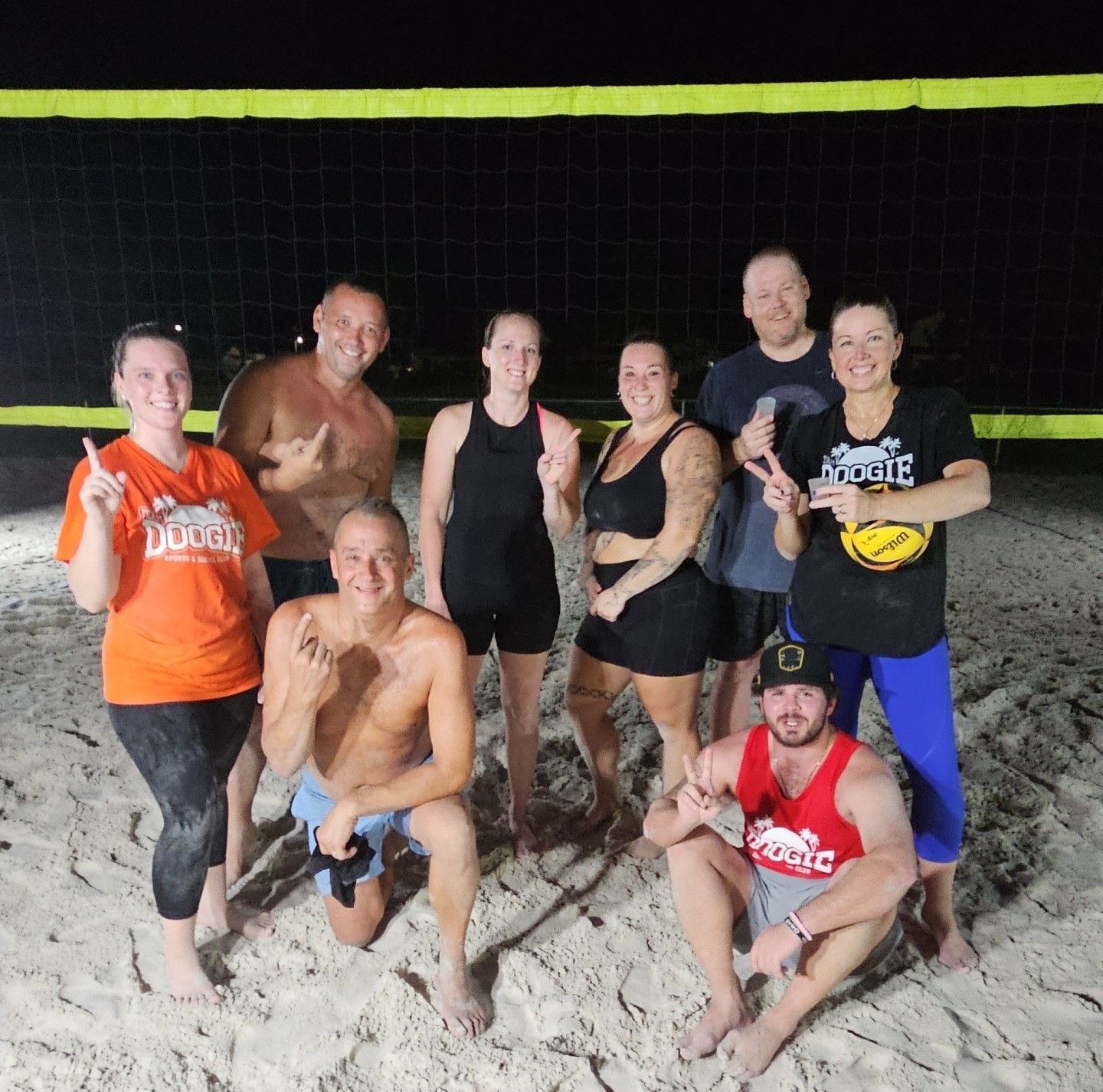 A group of people posing for a picture on a beach with one wearing an orange shirt that says ducks