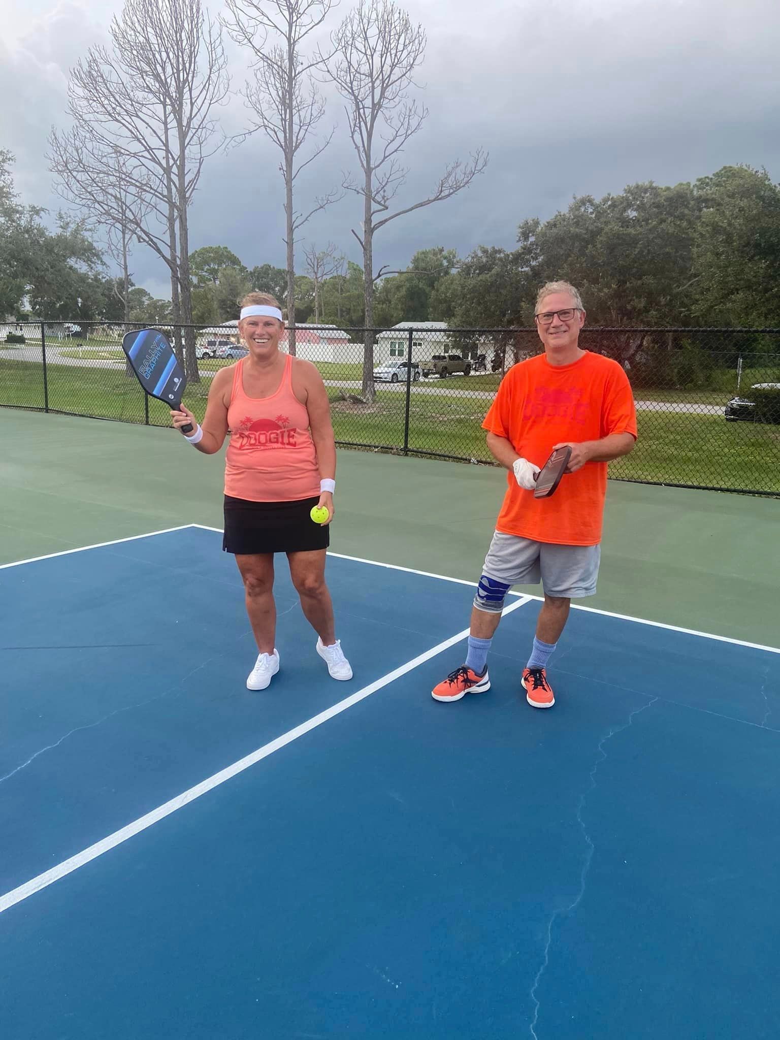 A man and a woman are standing on a tennis court holding tennis rackets.