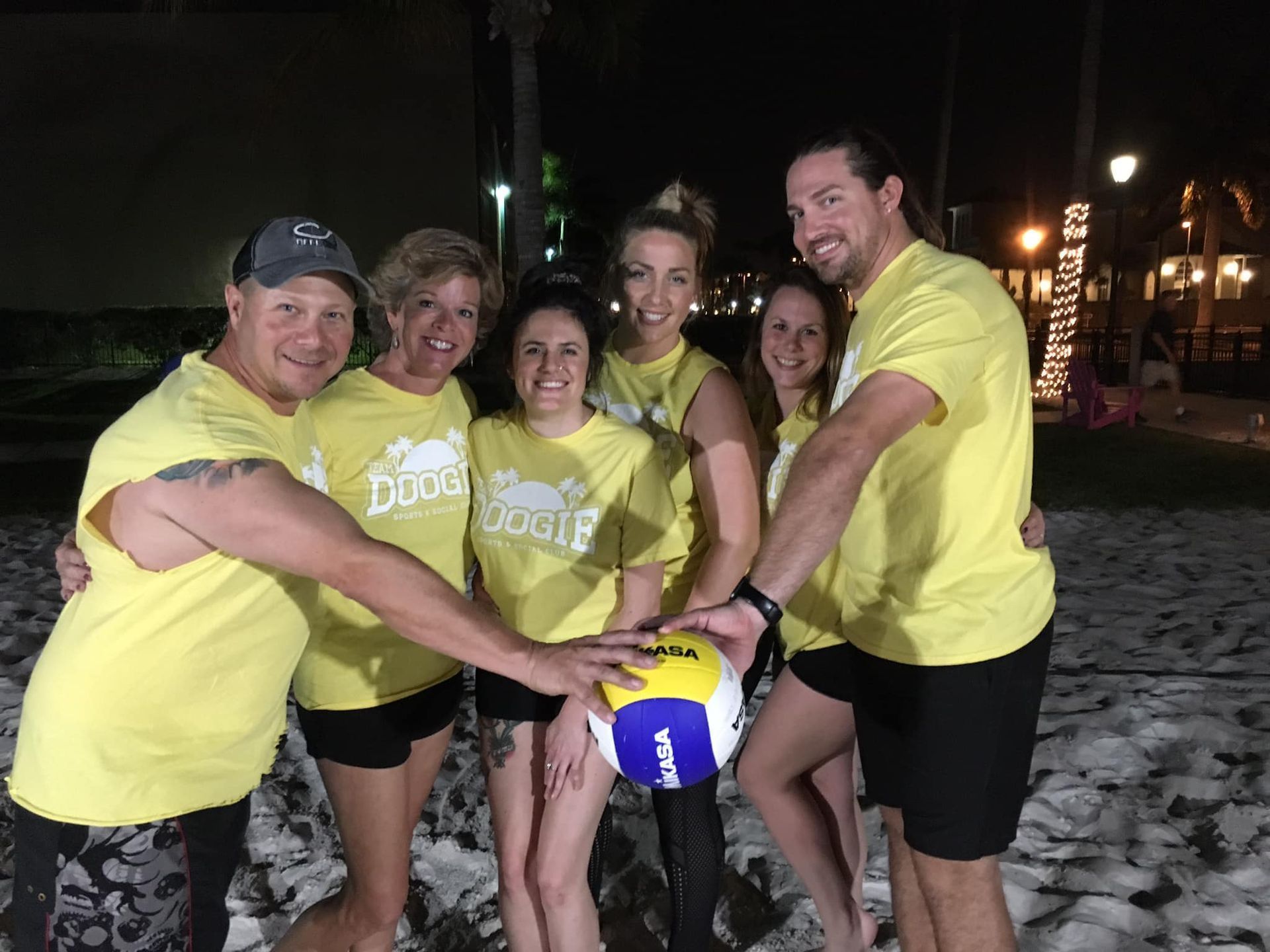A group of people wearing yellow shirts are holding a volleyball.