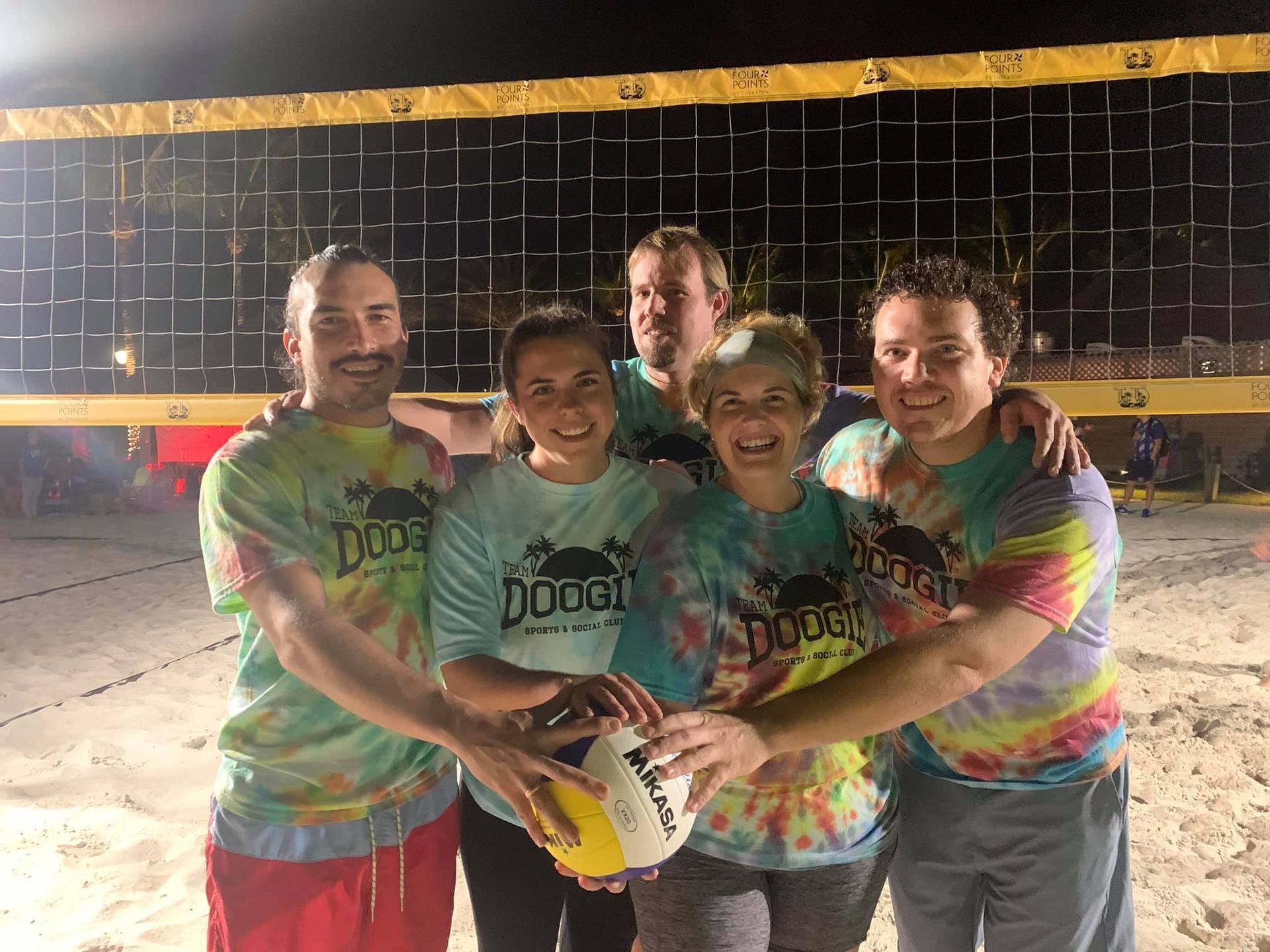 A group of people are posing for a picture on a beach holding a volleyball.