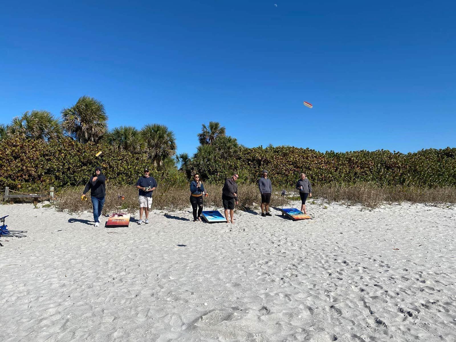 A group of people are playing cornhole on the beach.