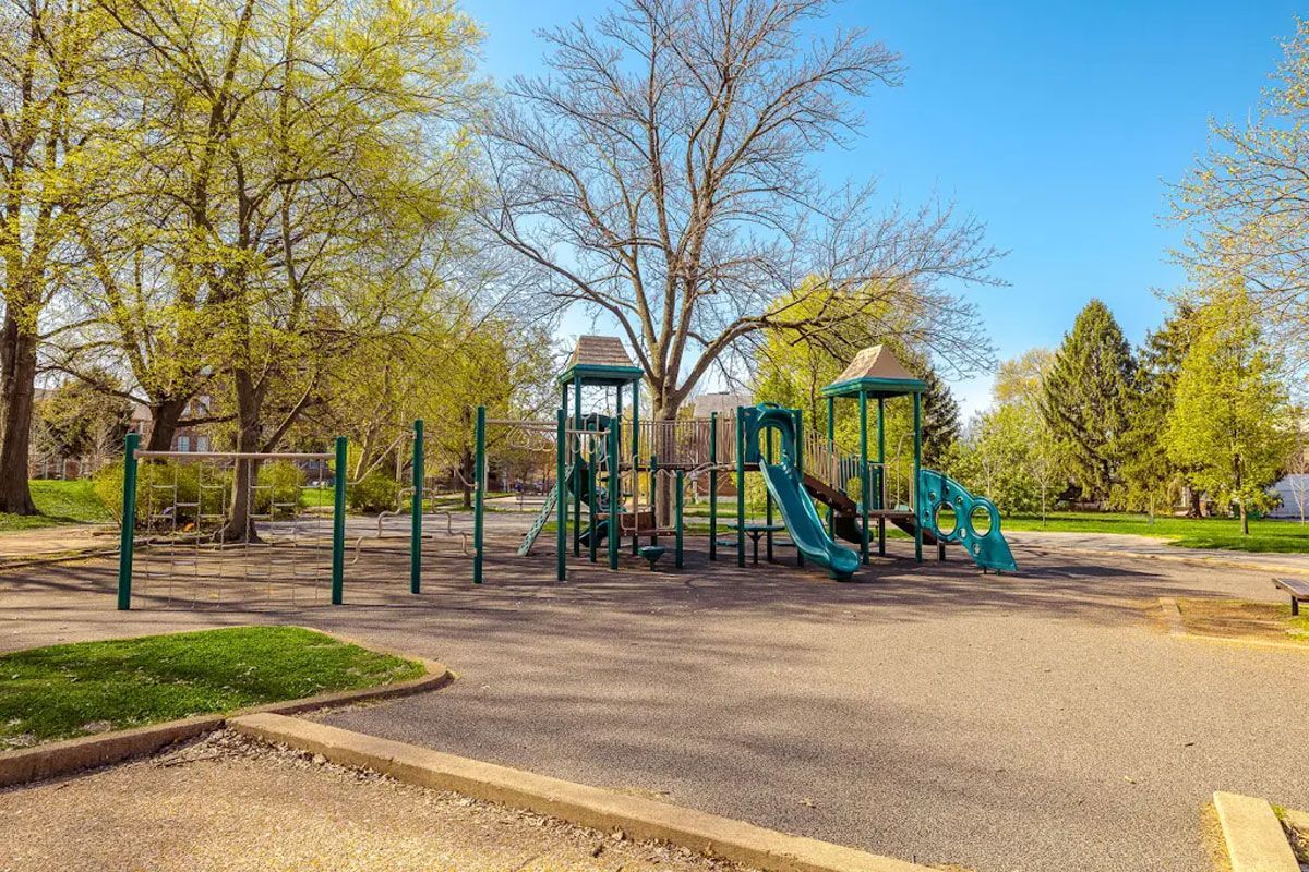 An empty playground in a park with trees in the background on a sunny day.