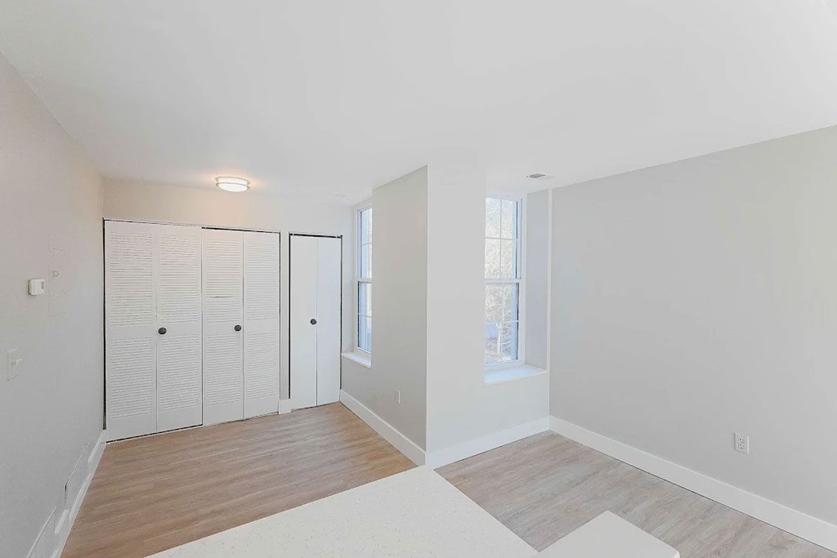 An empty room with white walls , wooden floors , and a window.