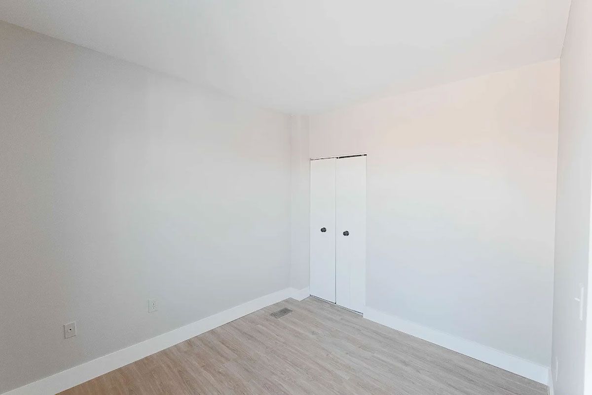 An empty bedroom with hardwood floors and white walls.