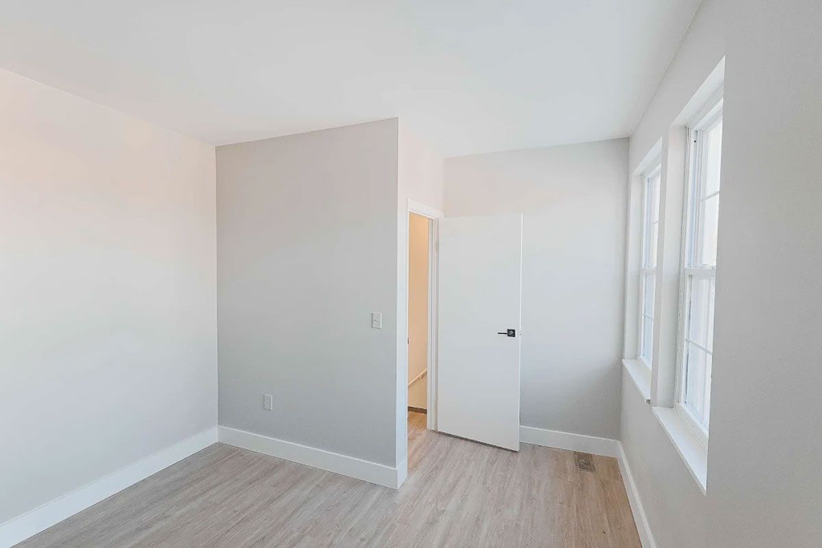 An empty bedroom with hardwood floors , white walls , and two windows.