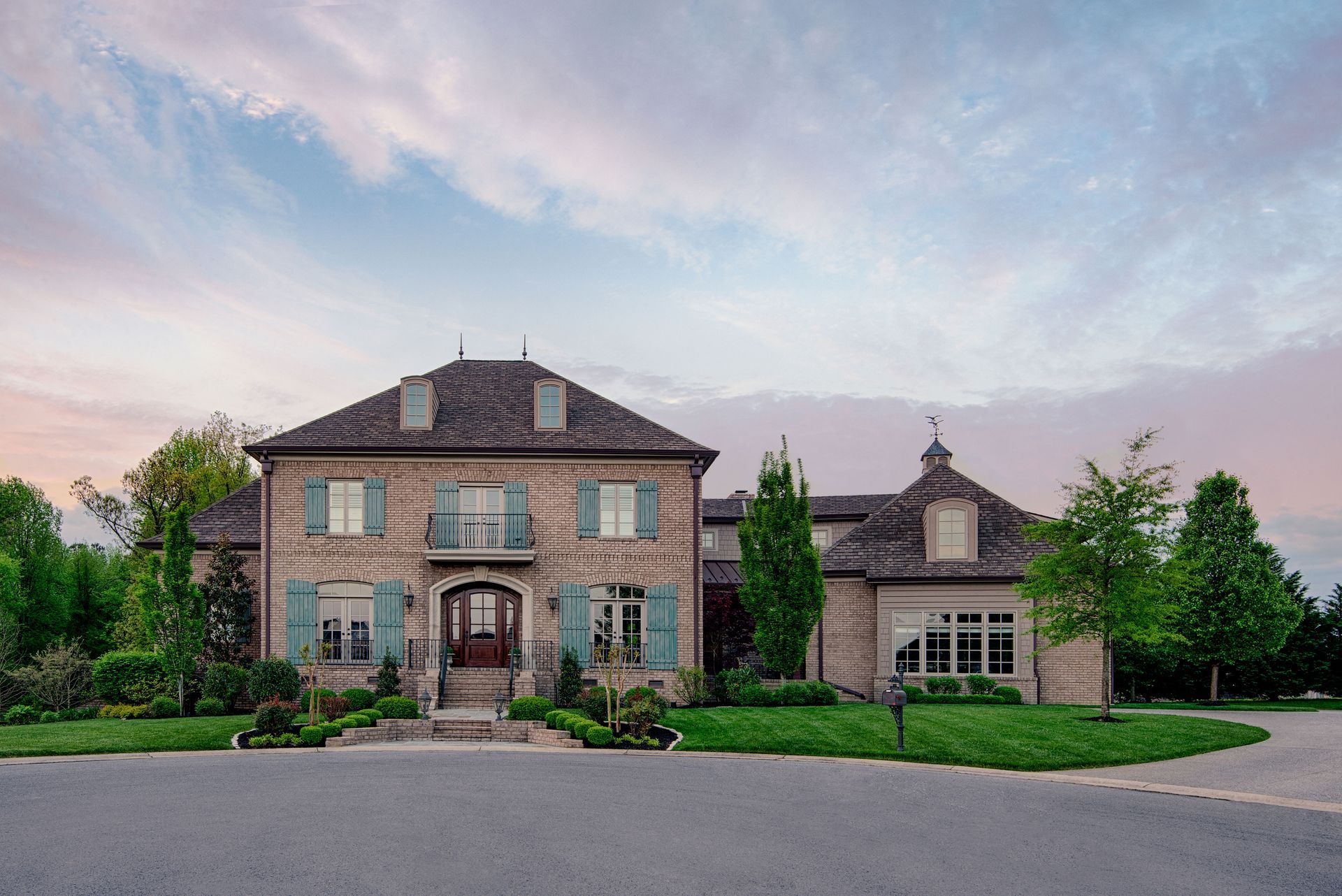 A large brick house with blue shutters is sitting on top of a lush green hillside.