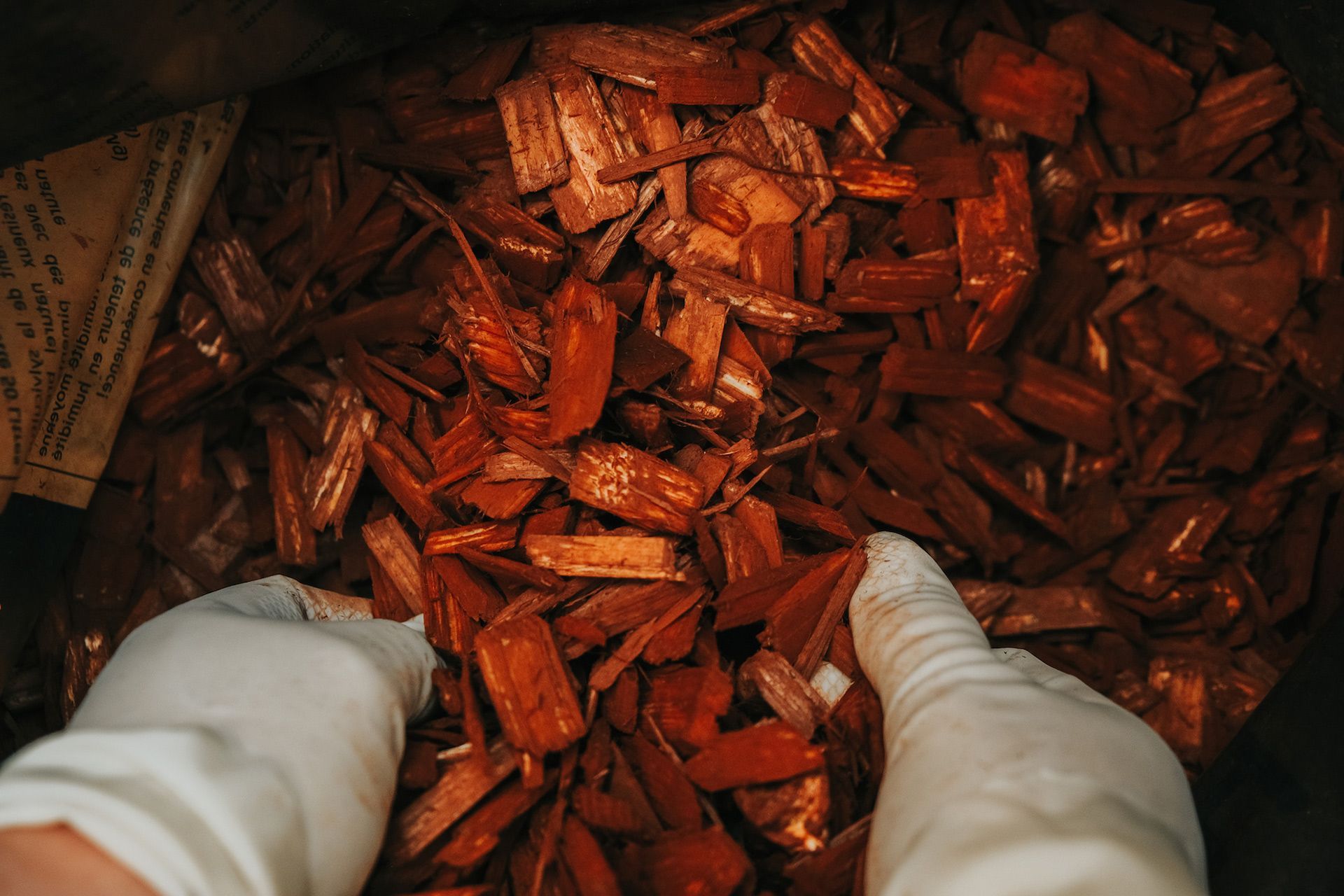 A person wearing white gloves is standing in a pile of wood chips.
