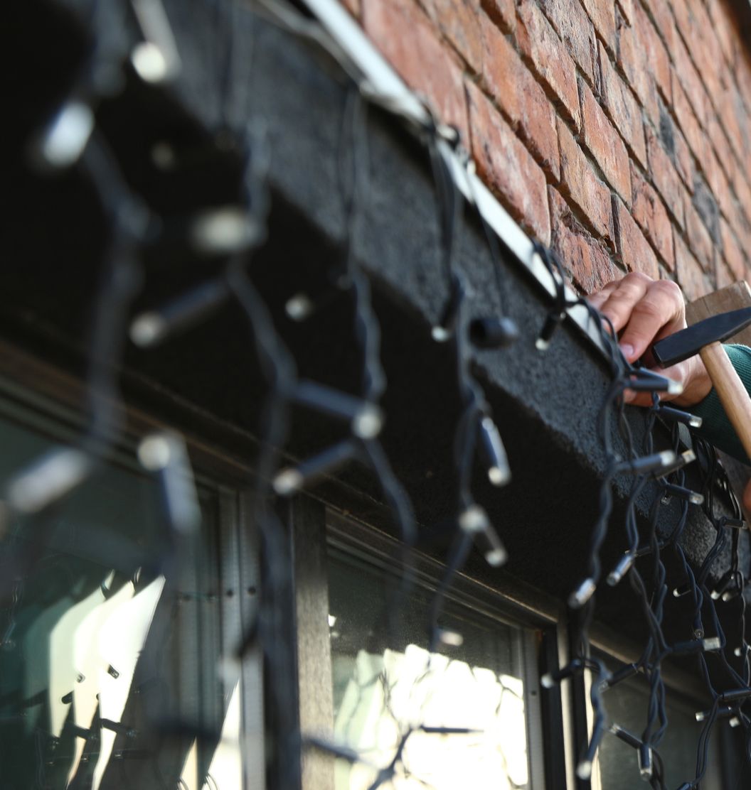 Person installing black Christmas lights on the edge of a brick building.