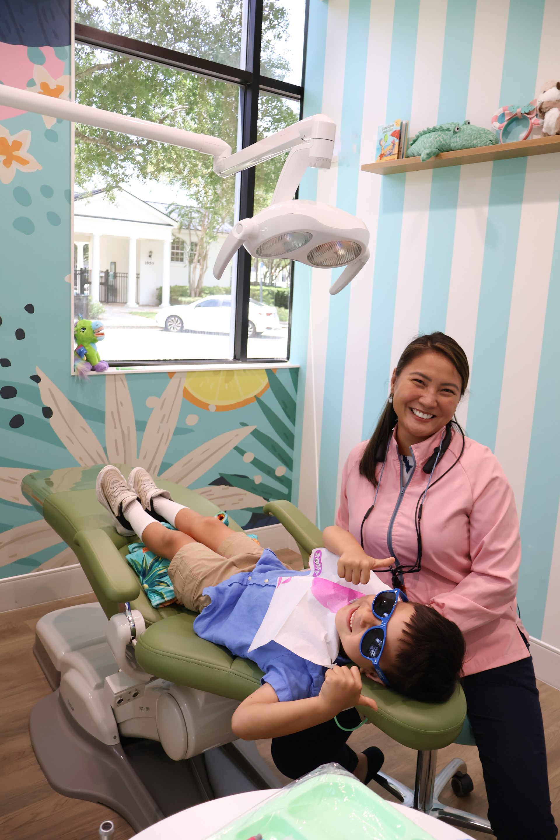 A child is sitting in a dental chair while giving thumbs up and smiling at the camera along with the dentist