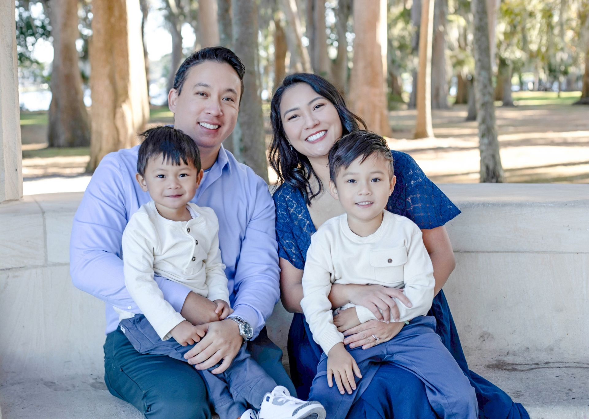 A family is posing for a picture while sitting on a bench in a park.