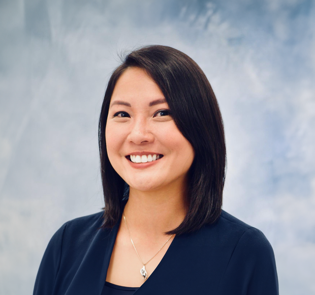 A woman wearing a black jacket and a necklace is smiling for the camera.