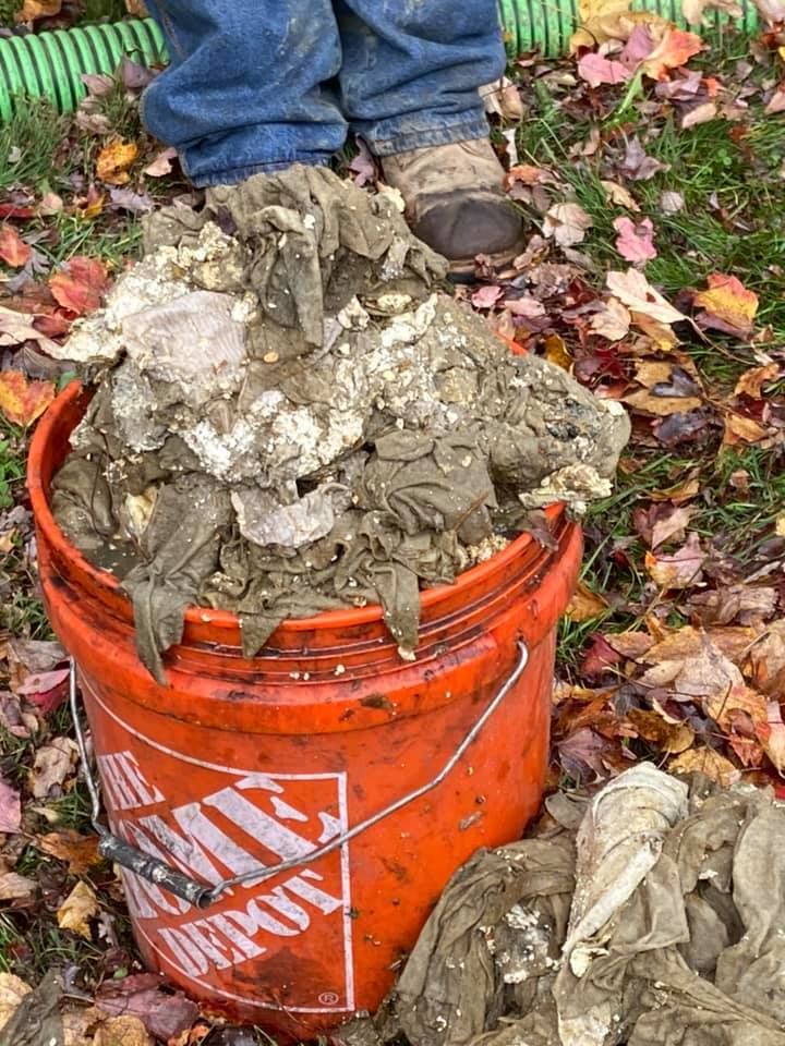 A person is standing next to a bucket filled with dirt and leaves.