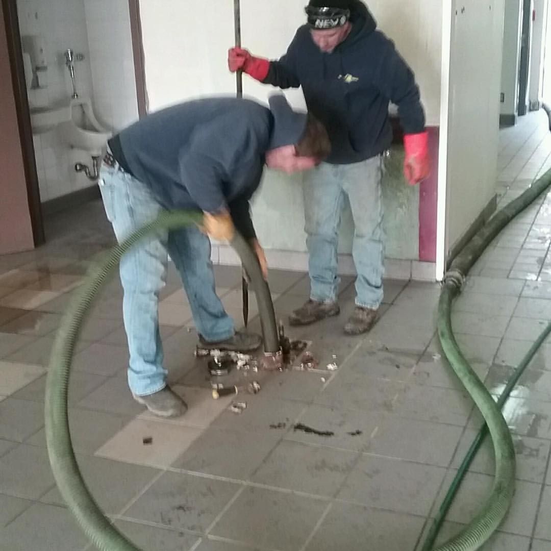 Two men are working on a drain with a hose