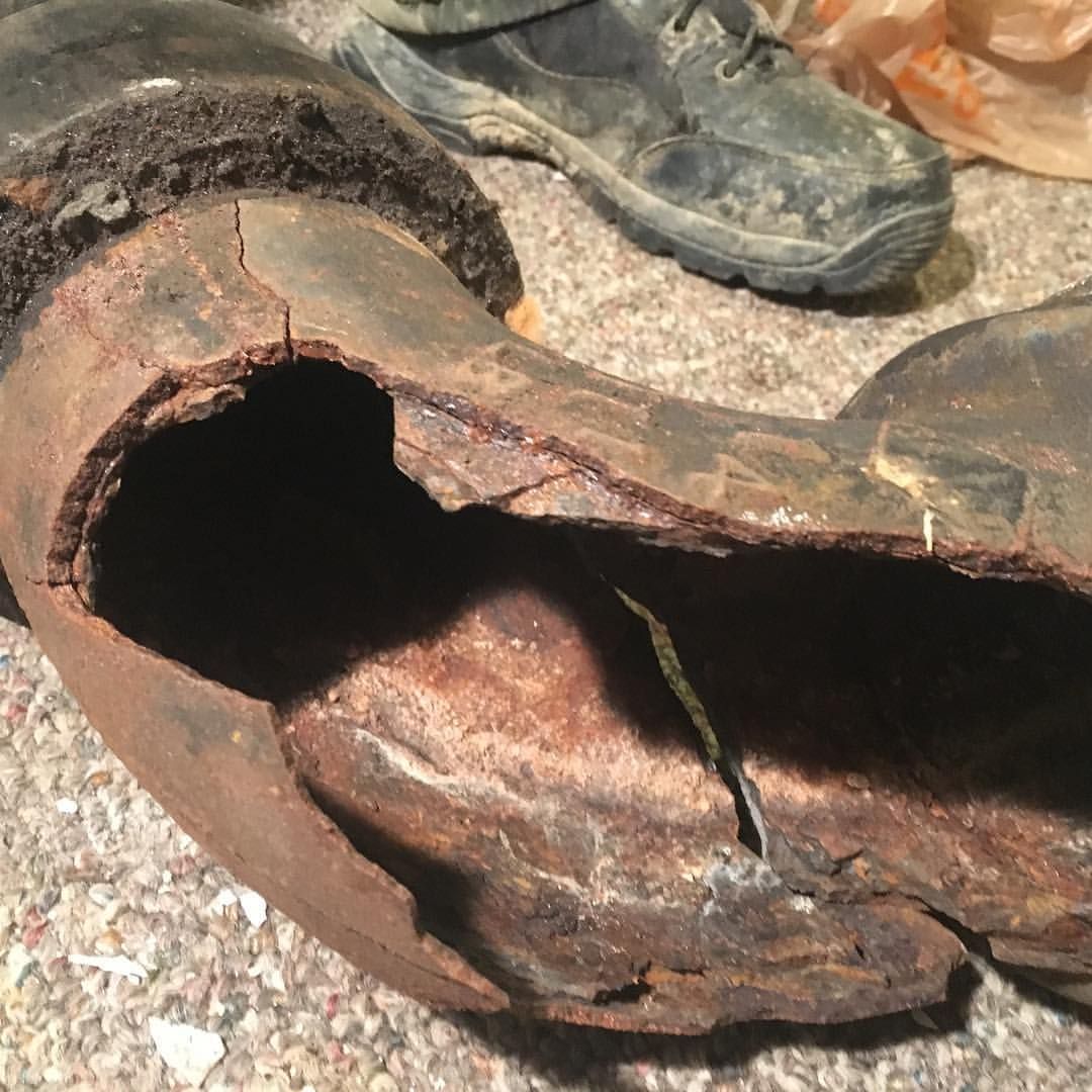 A broken boot is laying on the ground next to a pair of shoes