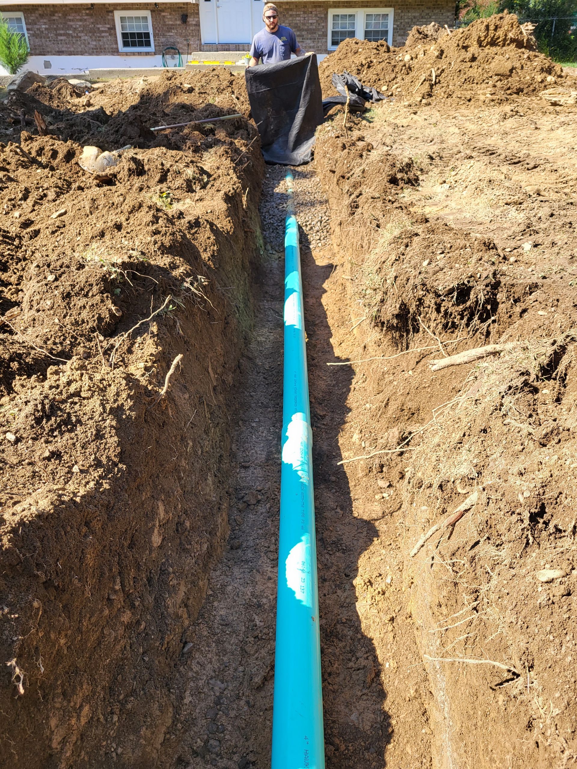 A man is standing in the dirt next to a blue pipe.