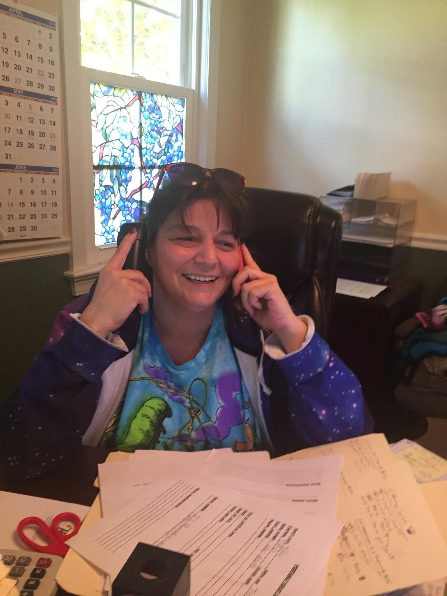 A woman is sitting at a desk talking on a cell phone