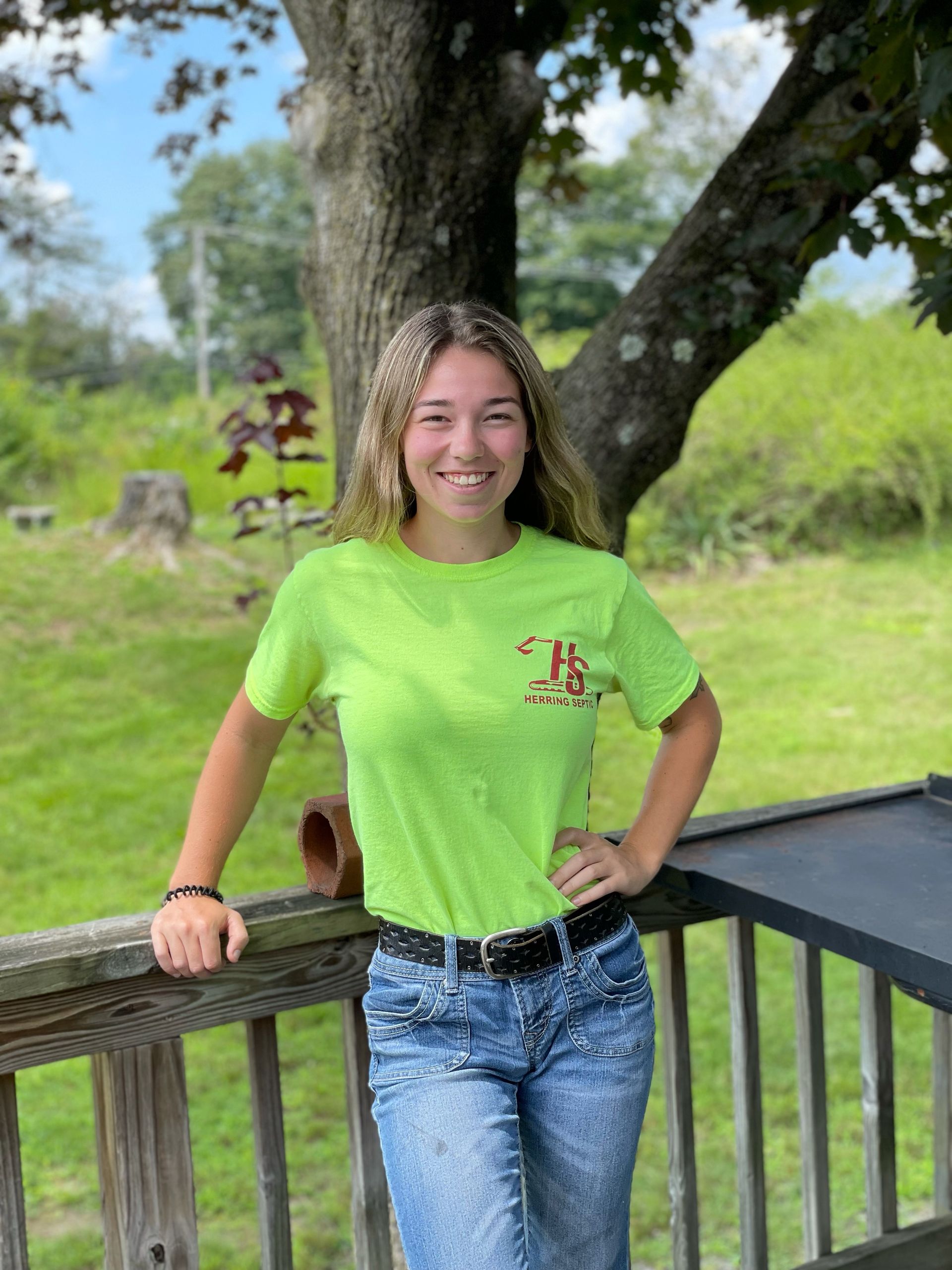 A woman in a neon green t-shirt and jeans is leaning on a wooden railing.