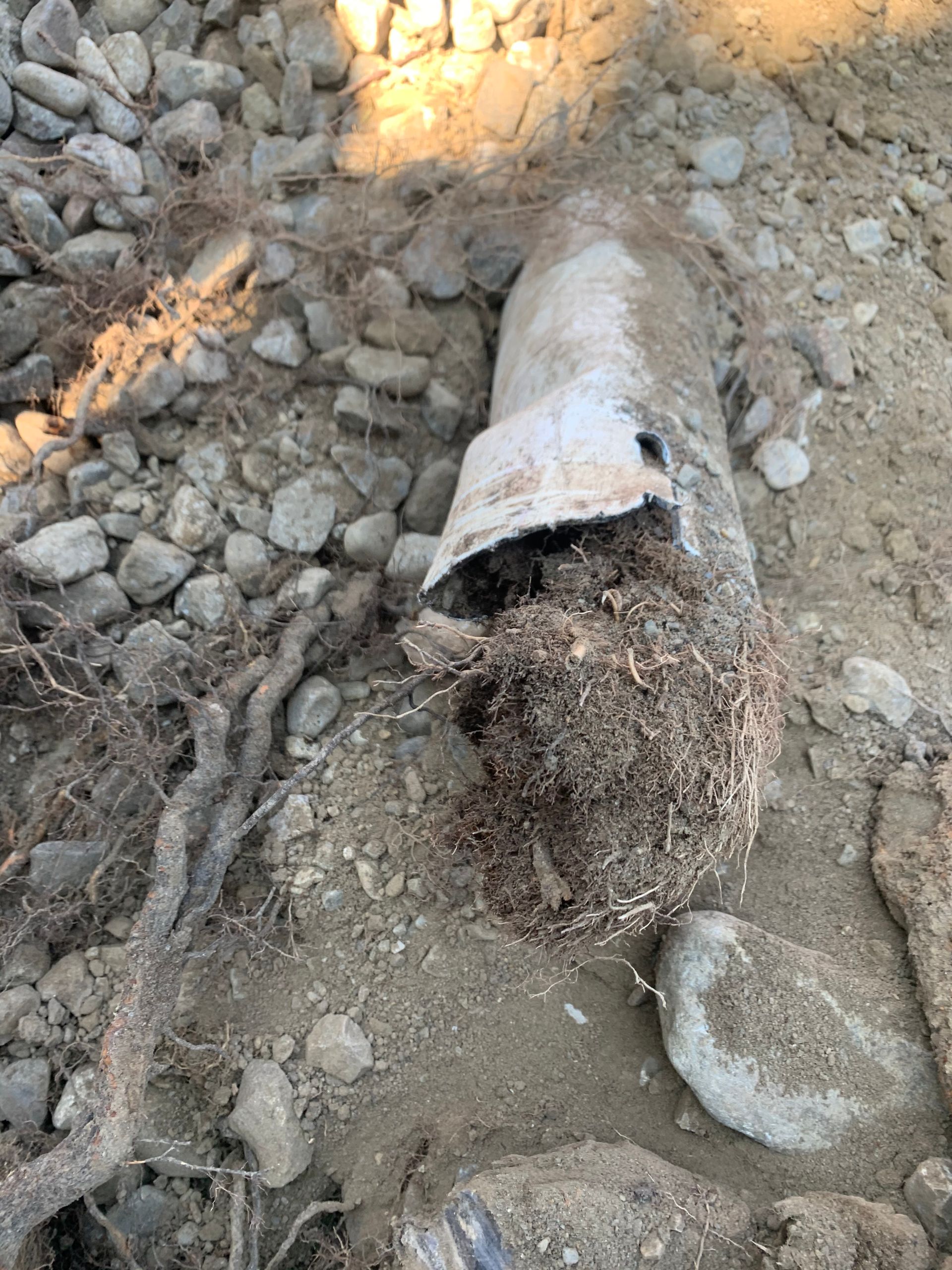 A metal pipe is laying on the ground next to rocks.