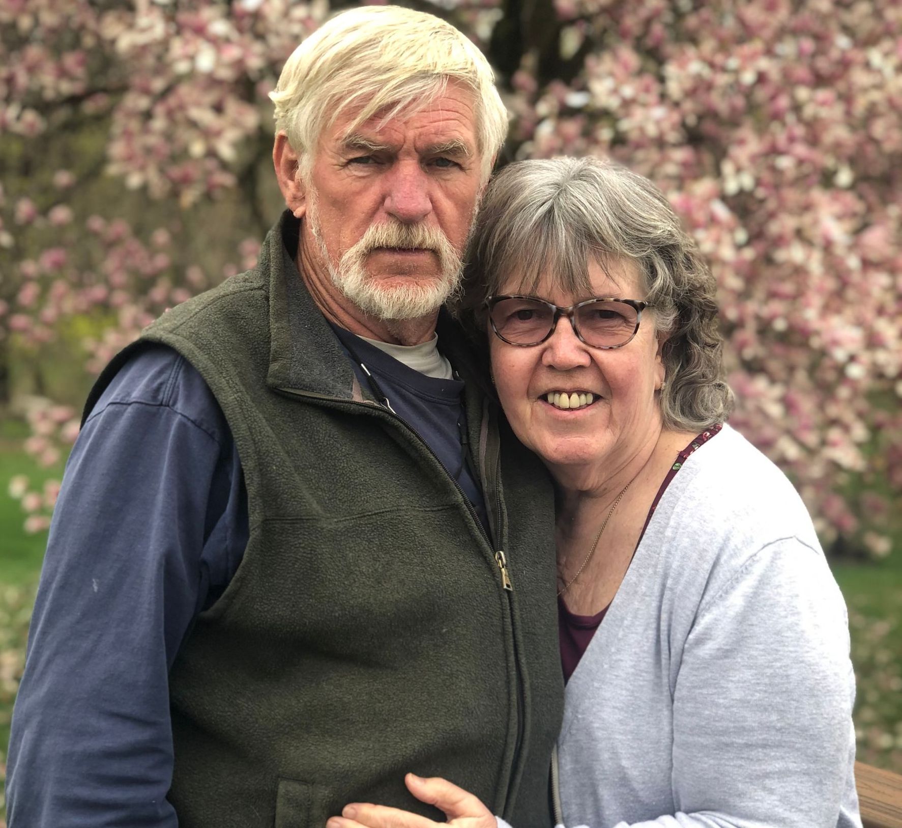 A man and a woman are posing for a picture in front of a flowering tree.