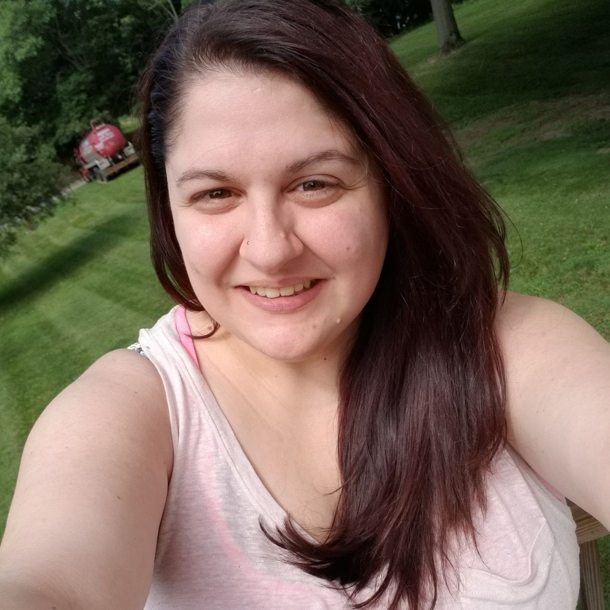 A woman in a white tank top is taking a selfie in a park.