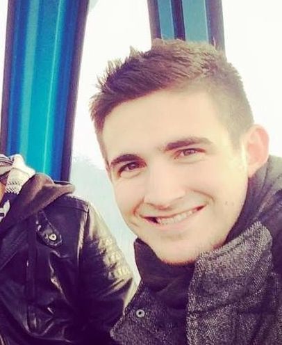 A young man in a black jacket is smiling for the camera