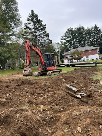 An excavator is digging a hole in the dirt in front of a house.