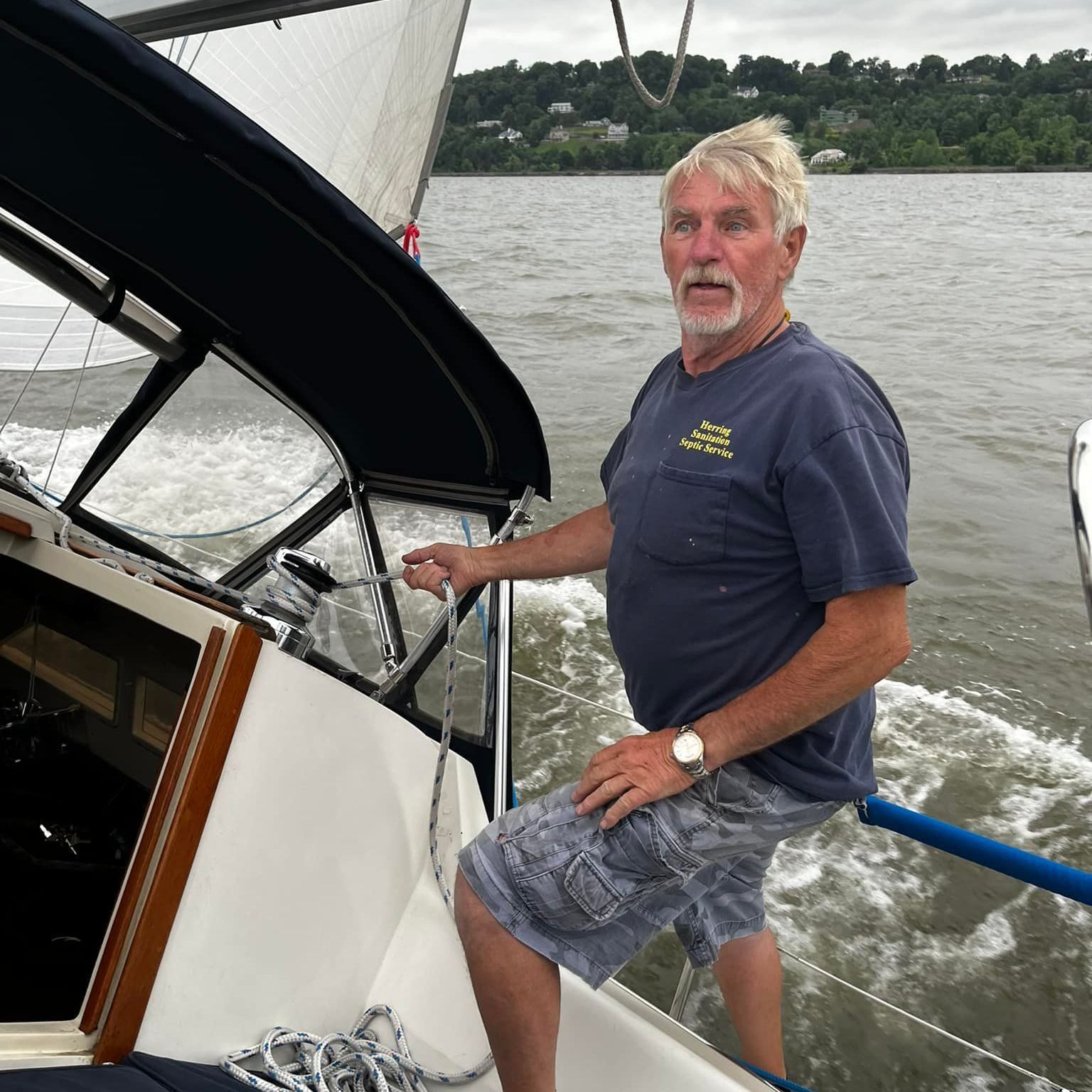 A man is sitting on the side of a sailboat in the water.