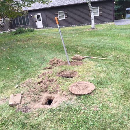 A manhole cover is sitting in the grass in front of a house.