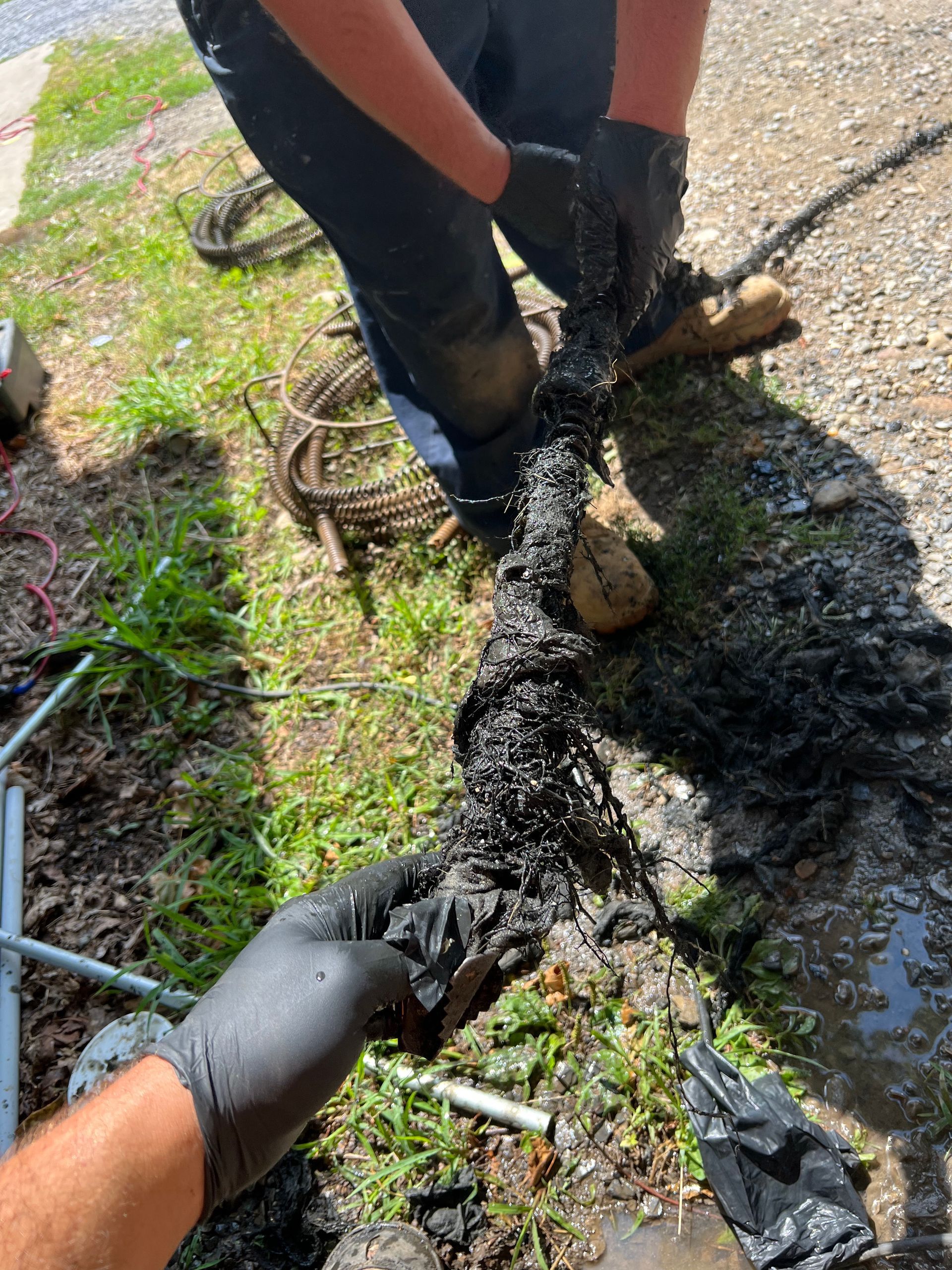 A man wearing black gloves is cleaning a drain.