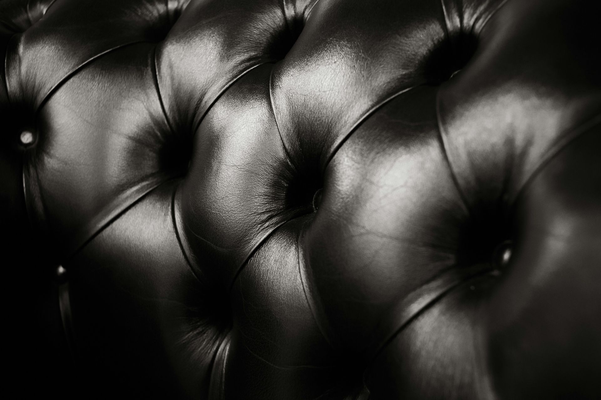 Close-up of black tufted leather upholstery with glossy highlights