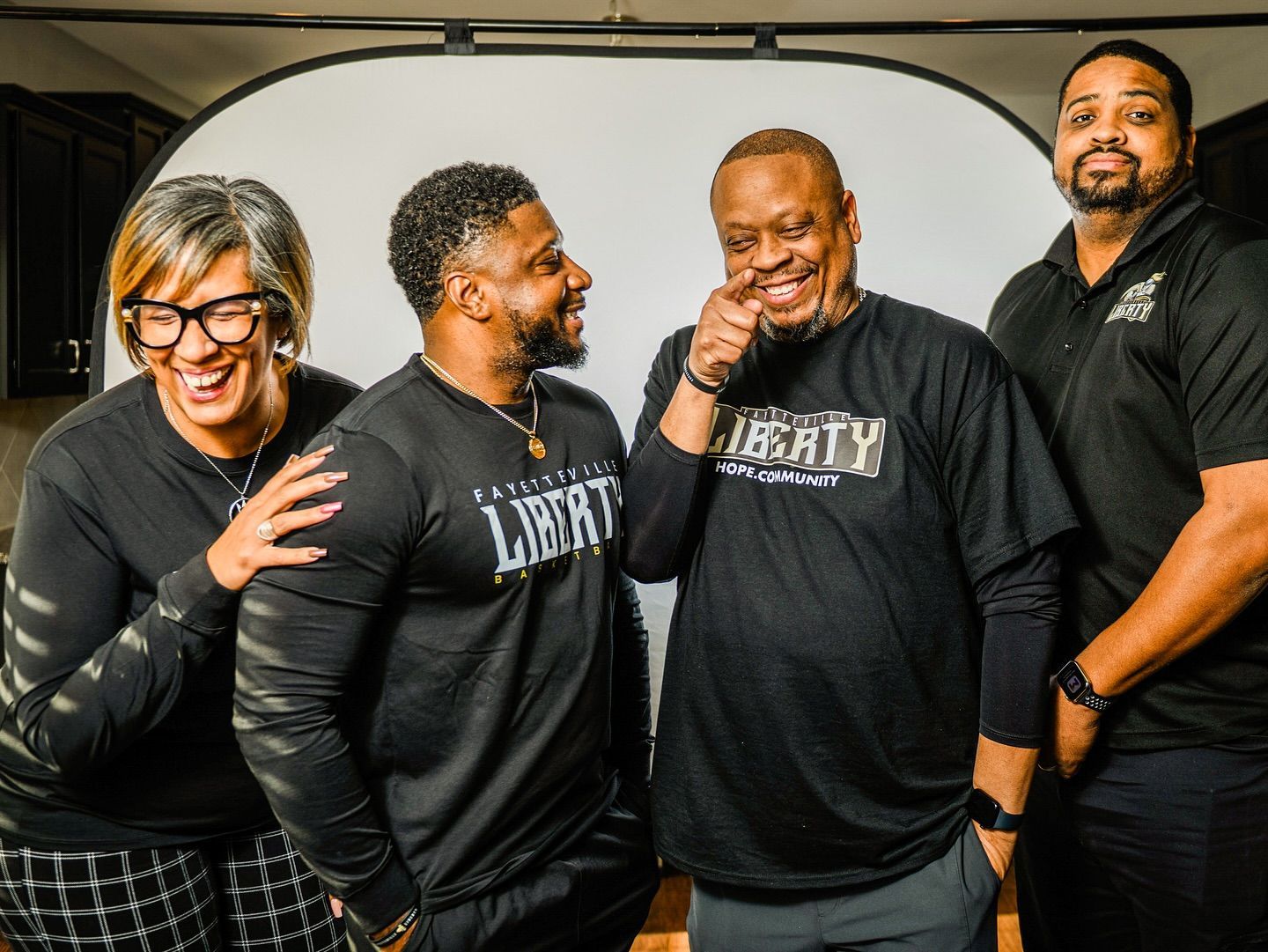 Four people in black Liberty shirts smiling, standing in front of a white backdrop.