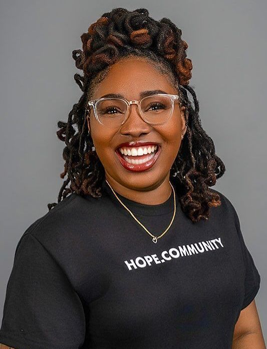 Black woman with locs smiles, wearing glasses and black shirt with