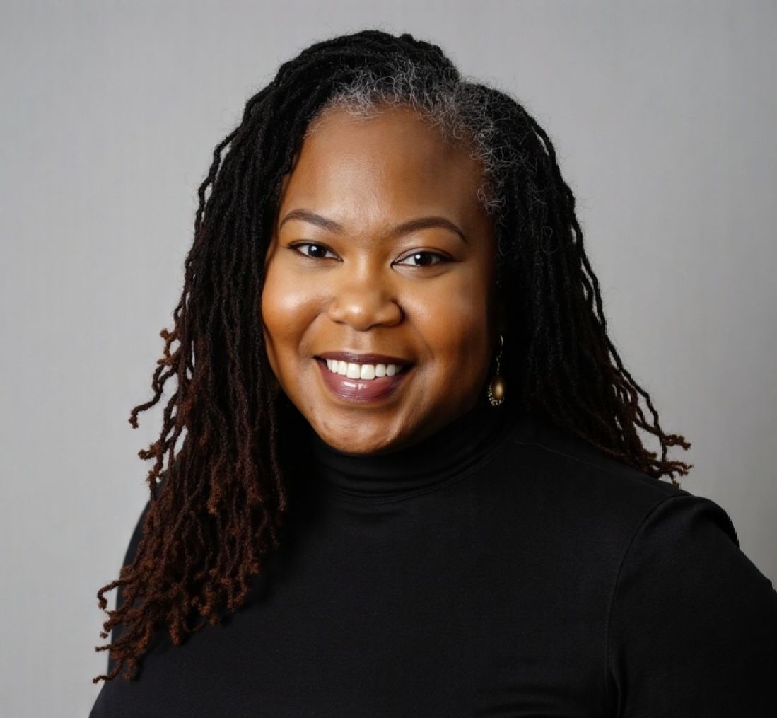 Smiling Black woman with locs, wearing a black turtleneck, against a gray background.