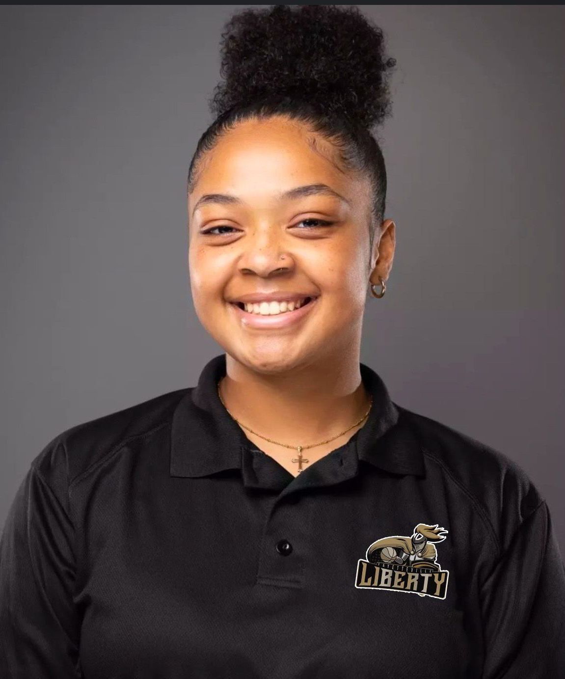 Young woman with bun smiling, wearing a black polo shirt with