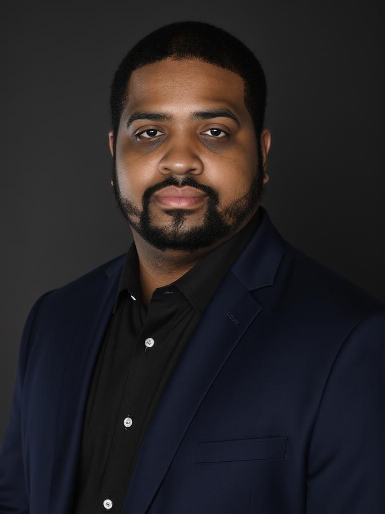 Man in a navy blue blazer, black shirt, with a beard, looking directly at the camera with a neutral expression.