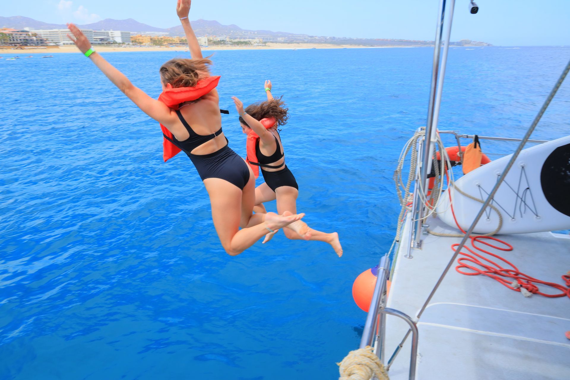 Two women are jumping off a boat into the ocean.