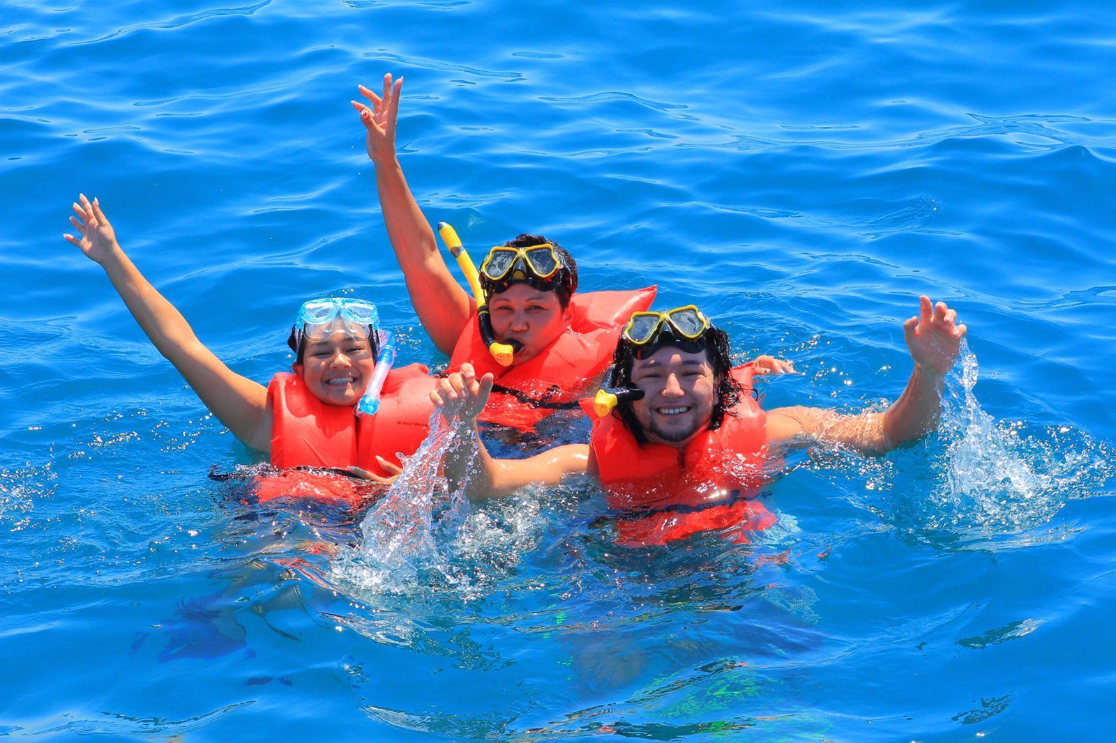 Tres personas nadan en el océano con los brazos en alto.