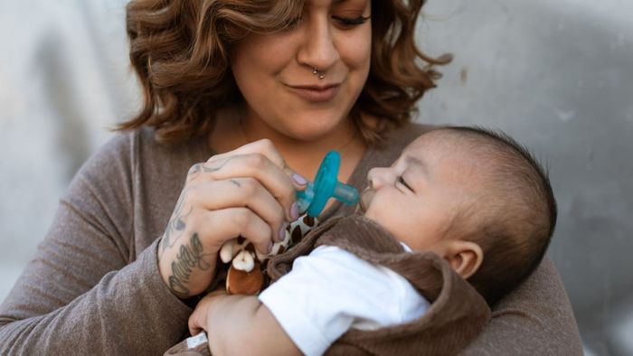 Una mujer sostiene a un bebé y le ofrece un chupete. 