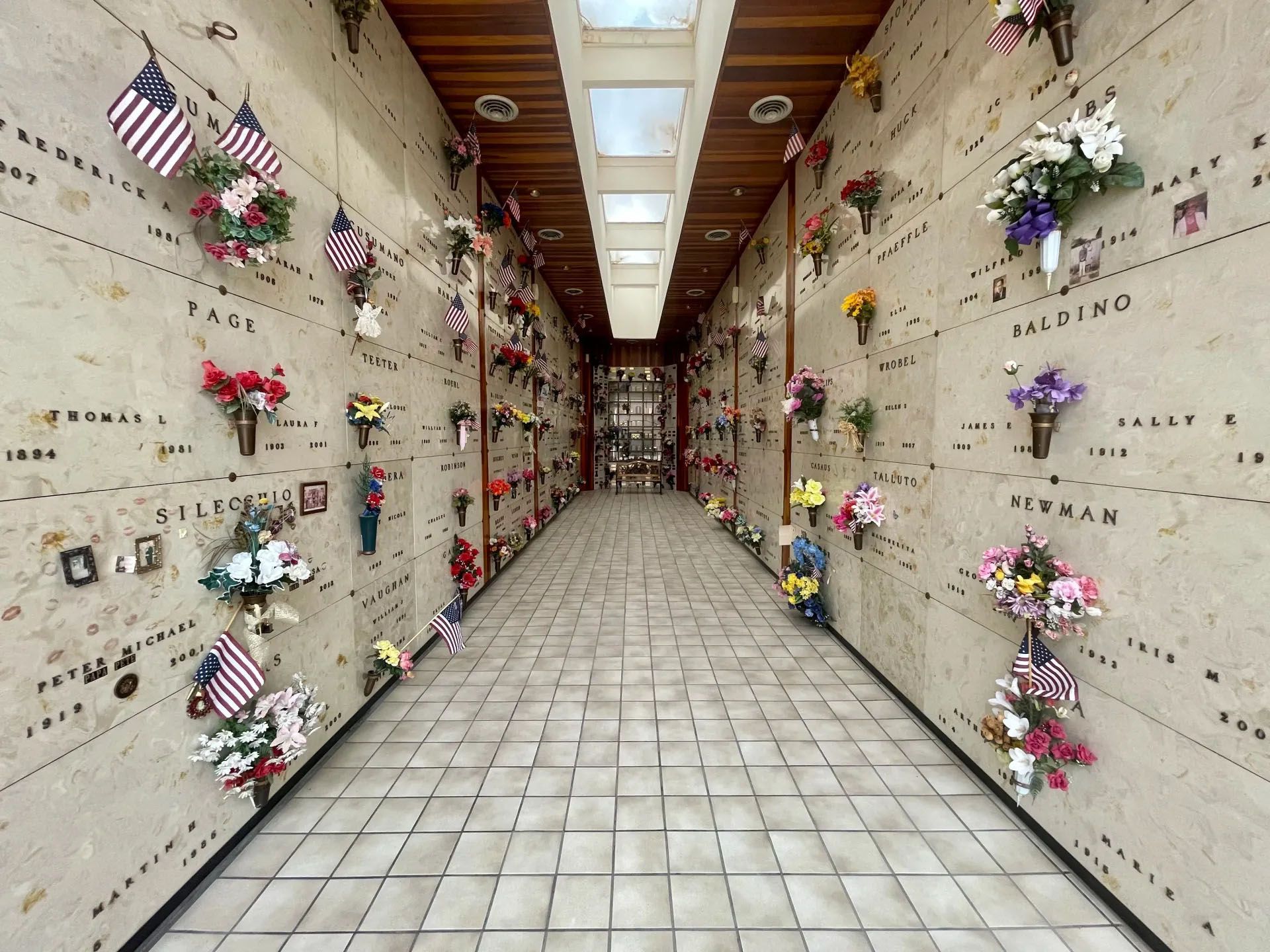 Interior of a mausoleum, long corridor with niches holding flowers and American flags.