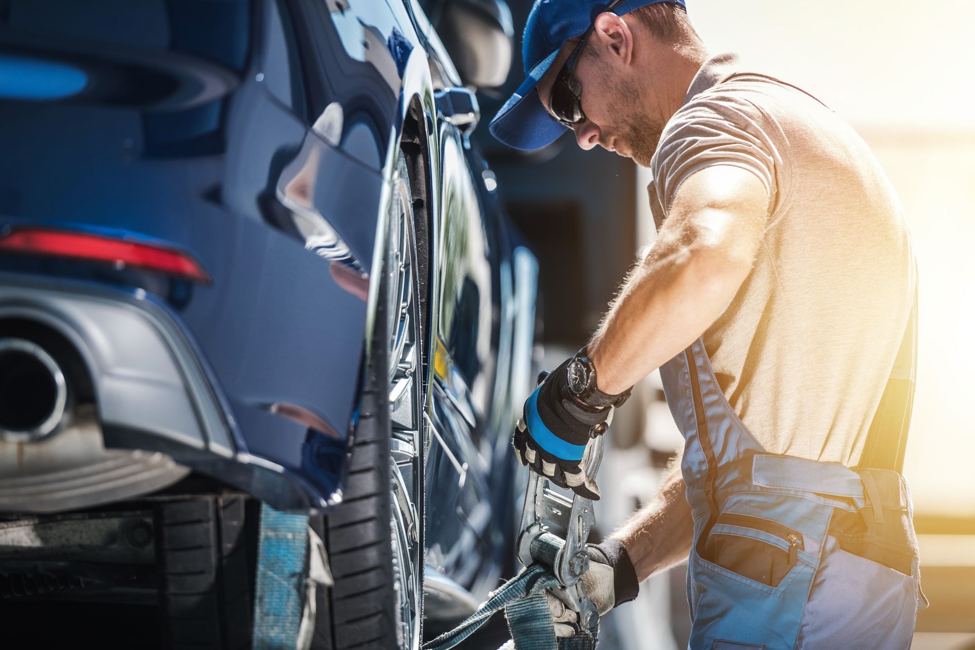 Worker securing a car onto a flatbed tow truck using safety straps. Worker securing a car onto a flatbed tow truck using safety straps.