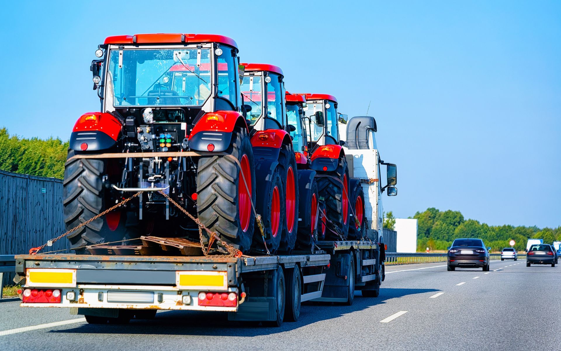 Heavy-duty truck used for towing red farming tractors, secured with metal chains for safety.