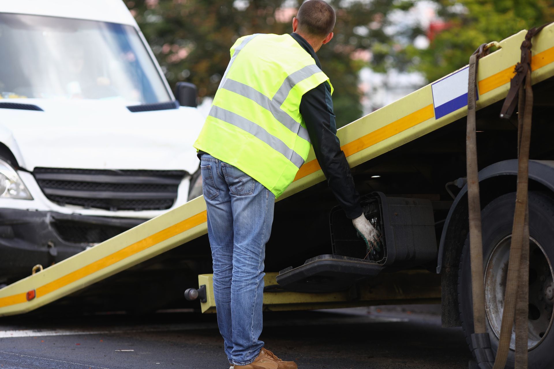 A man securing a car on a flatbed truck, illustrating an emergency towing service in action. A man securing a car on a flatbed truck, illustrating an emergency towing service in action.