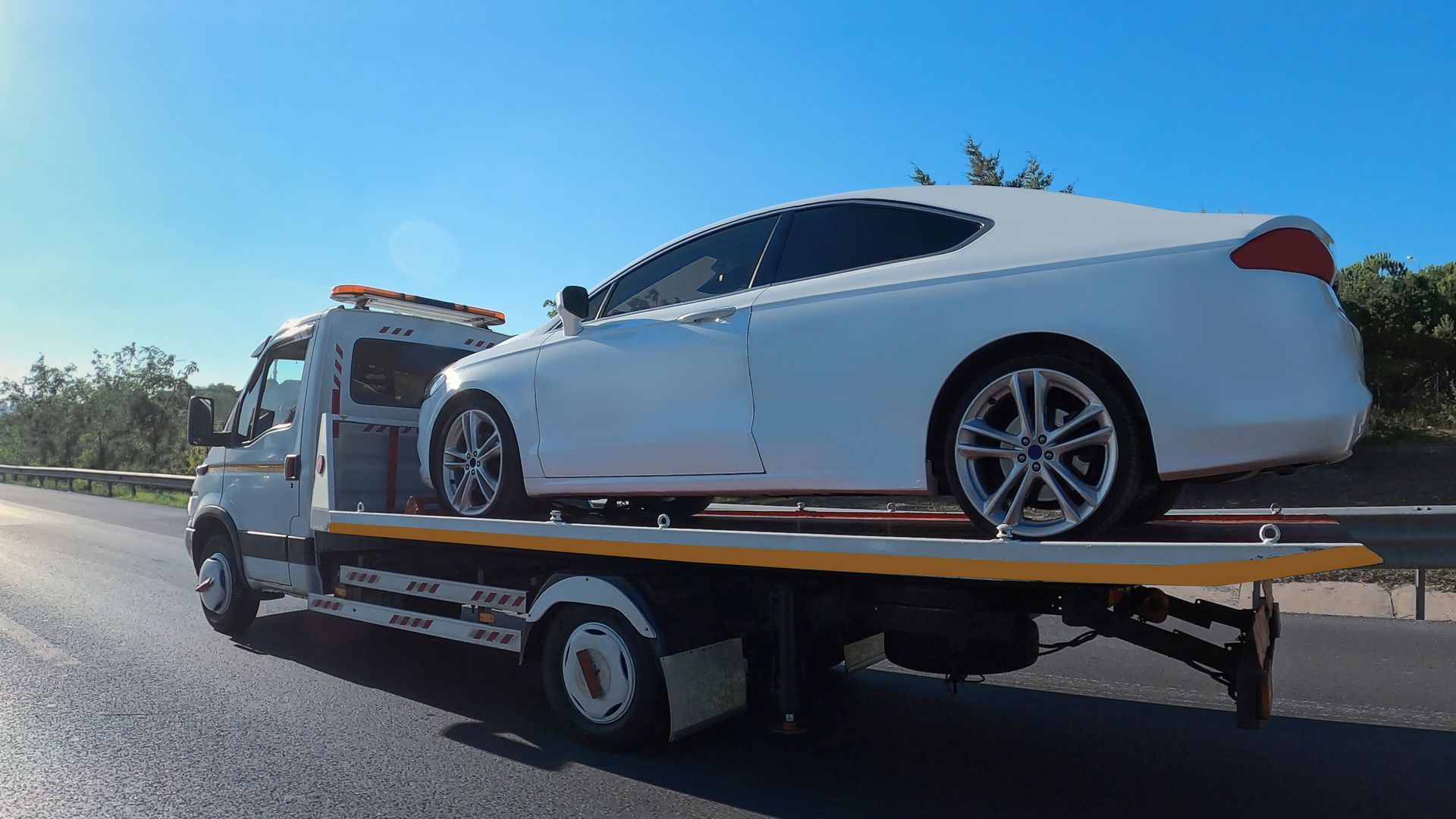 View of towing truck servicing a light grey car in the back on a road
