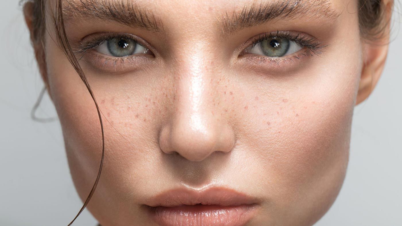 Close-up of a fair-skinned person with green eyes, freckles, and subtle makeup.