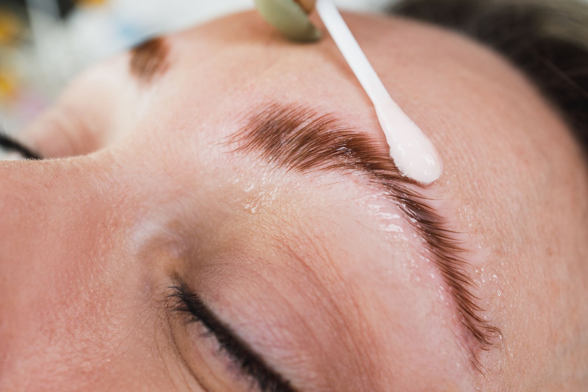 Person getting eyebrow tint applied with a cotton swab. Brown dye on eyebrows, close-up.
