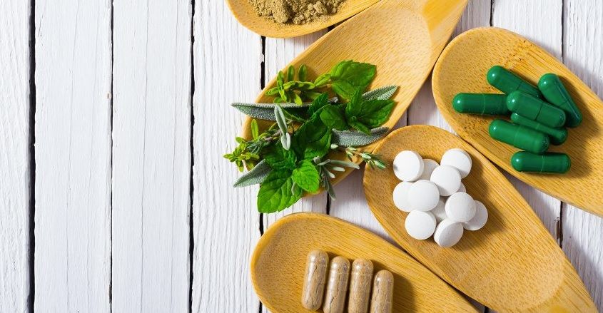 A wooden spoon filled with pills and herbs on a table.