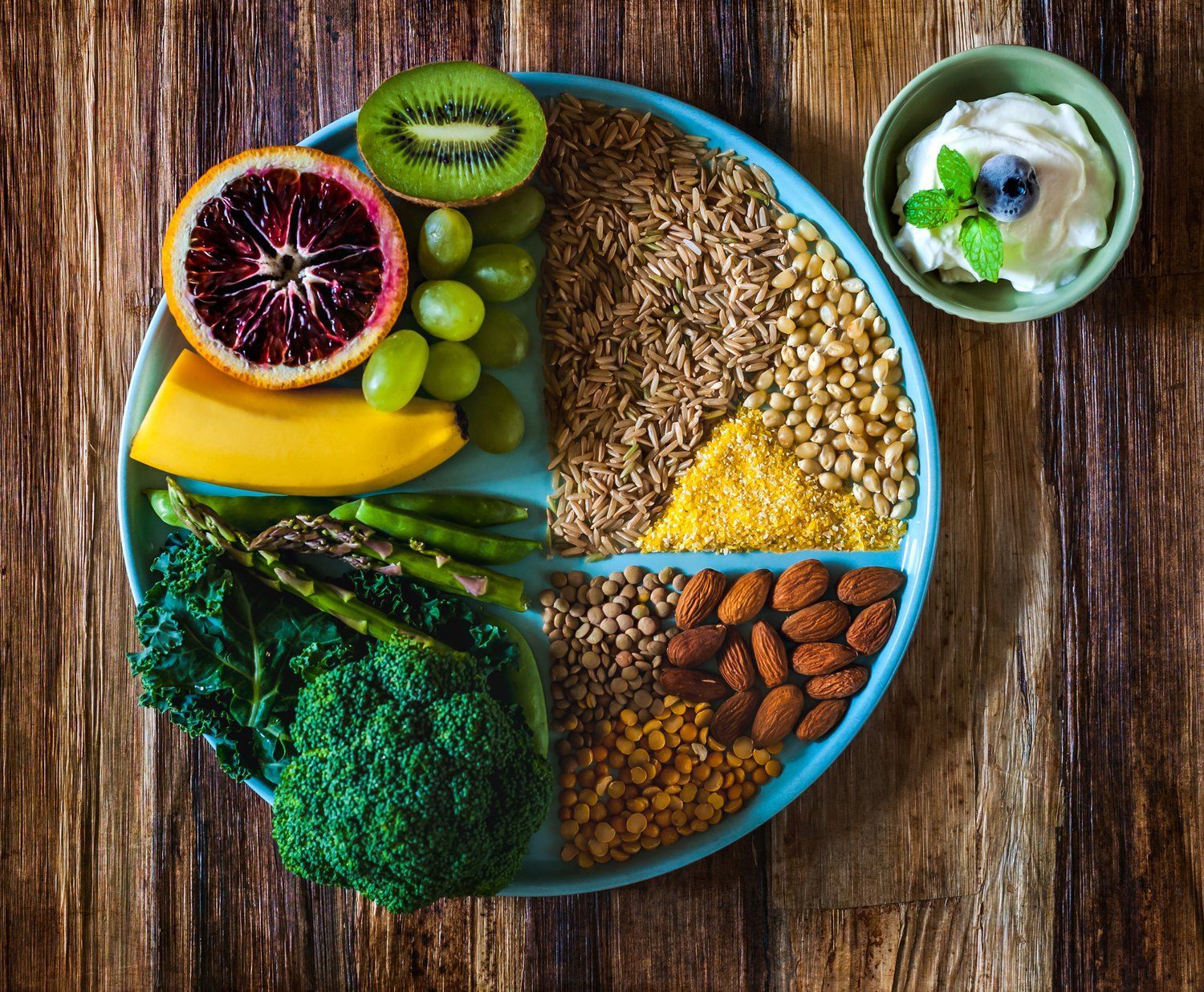 A plate of fruits , vegetables , nuts and yogurt on a wooden table.
