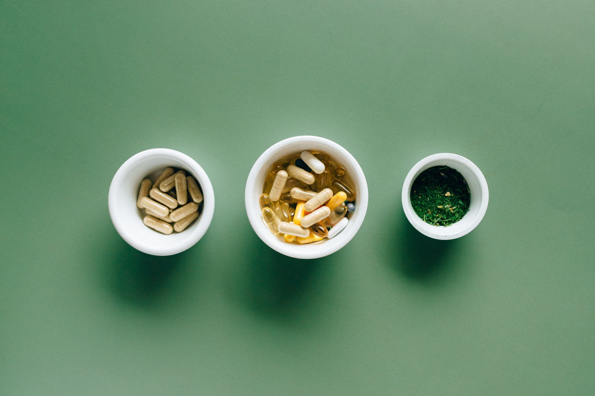 Three bowls filled with different types of pills on a green table.